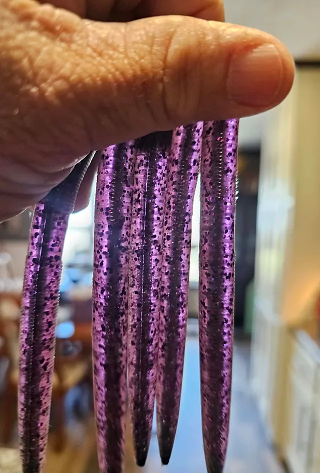 Purple stick worms with black flake and a darker core down the middle, hanging from a hand